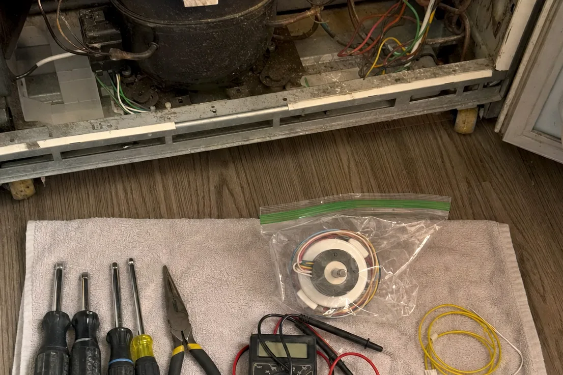 Hand tools and test leads on a towel, the open underside of a refrigerator behind them