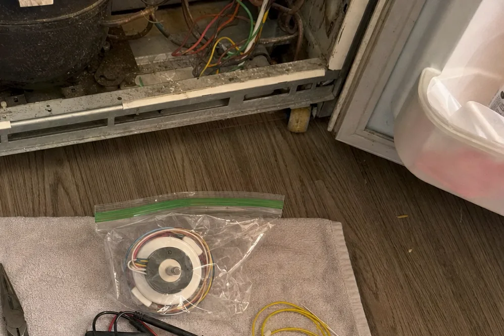 A coil of copper tubing and a bagged fan motor sitting beside the open base of a refrigerator